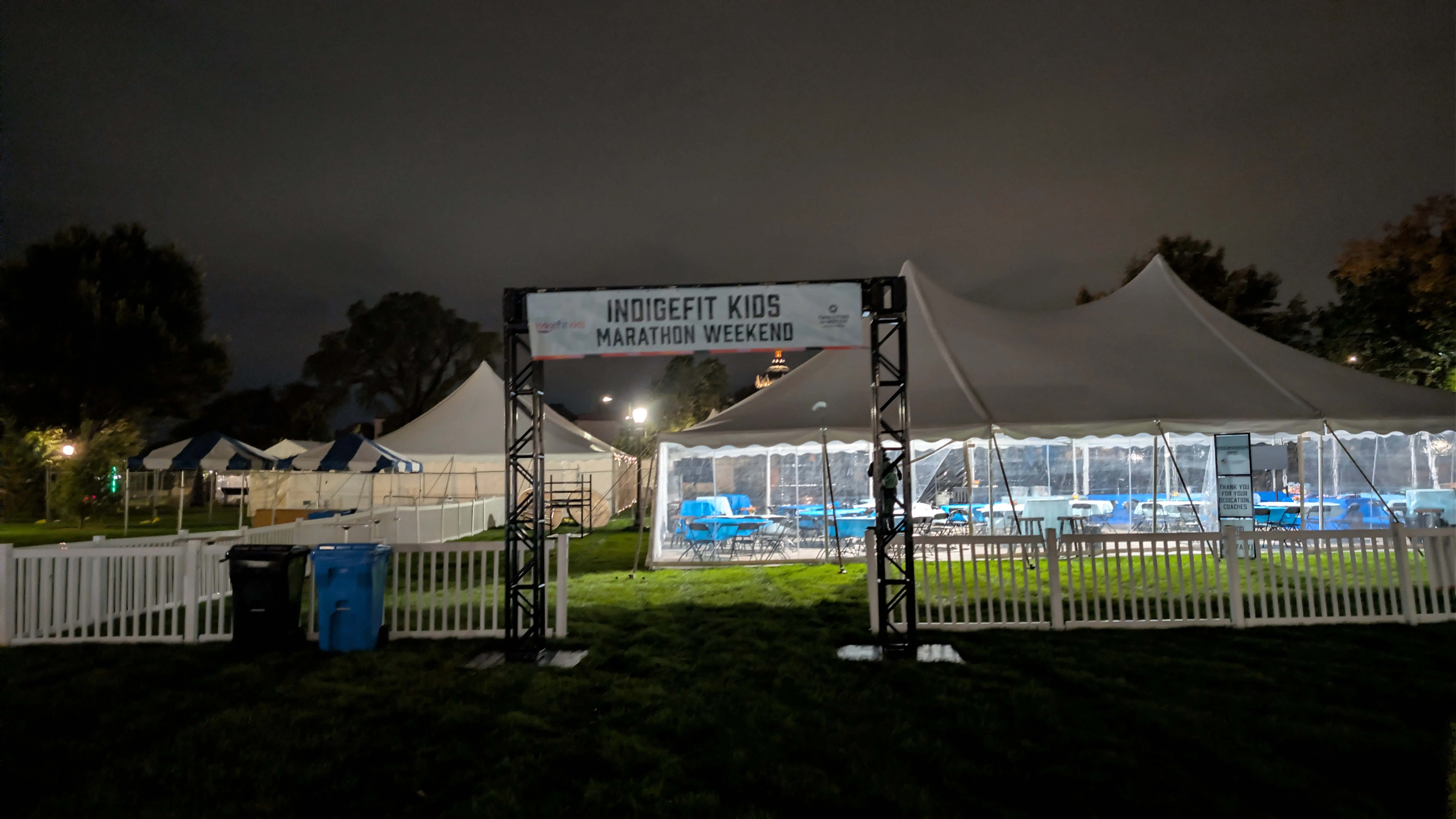 The Indigefit Kids Marathon Weekend banner over the entrance to a tent area near the State Capitol before sunrise