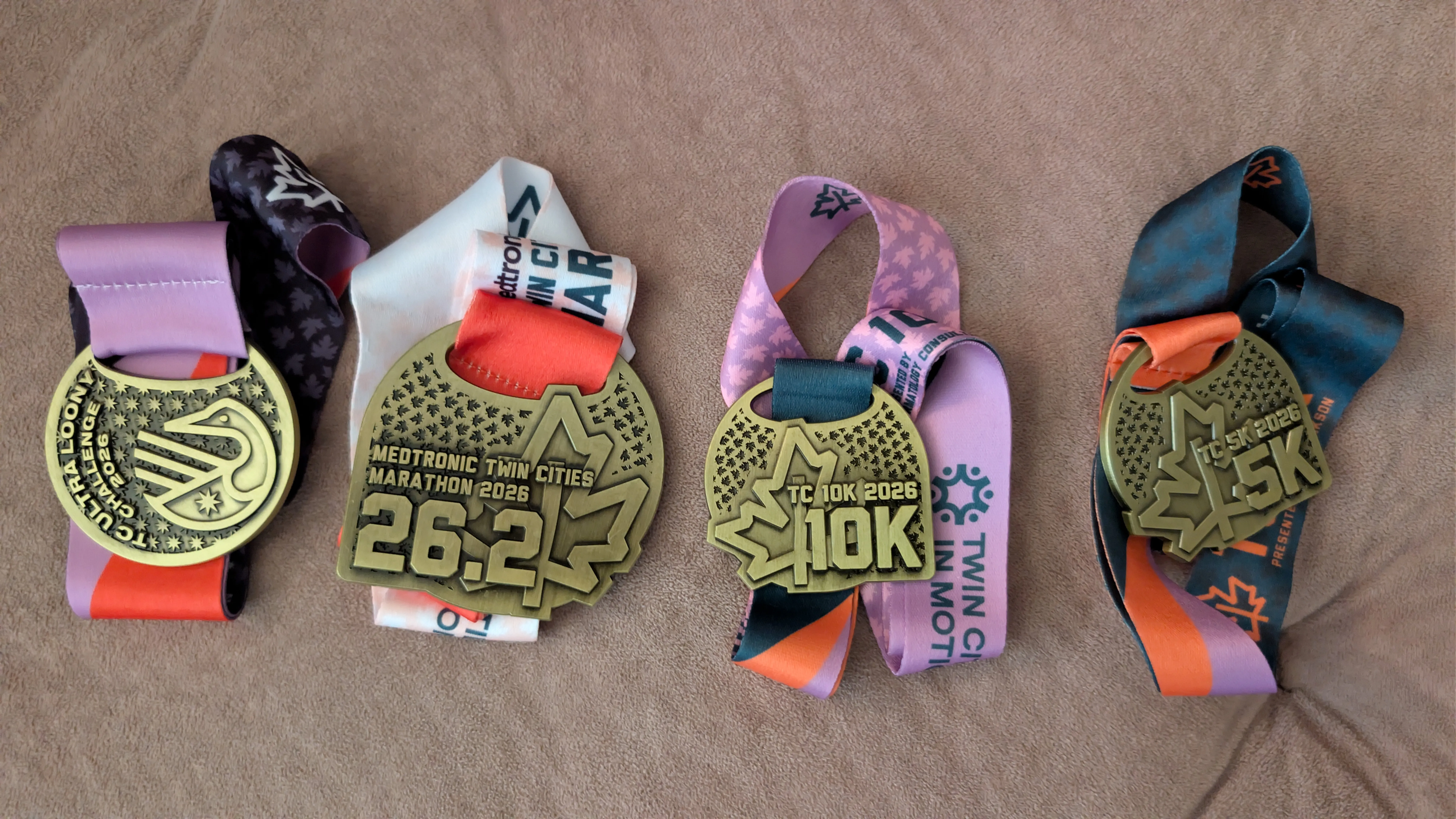 The four 2026 Twin Cities medals laid out side by side: Ultra Loony Challenge, marathon 26.2, 10K and 5K